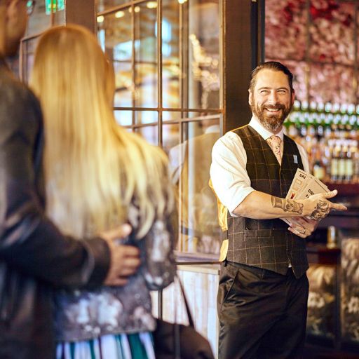Bartender greeting a man and women into restaurant setting with a friendly smile