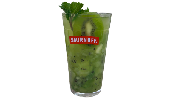 Copo alto com logo vermelho da Smirnoff contendo um coquetel verde refrescante repleto de pedaços e sementes de kiwi. A bebida é decorada com uma fatia inteira de kiwi no interior e um ramo de hortelã no topo da borda. Fundo branco isolado.