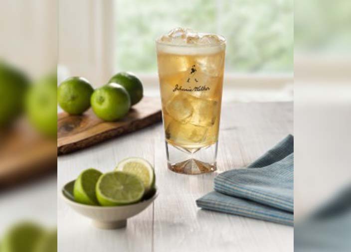 A highball glass of whisky and ginger surrounded by limes.
