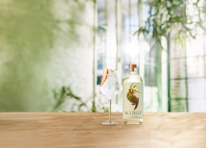 Bottle of Seedlip Spice 94 on table beside cocktail 