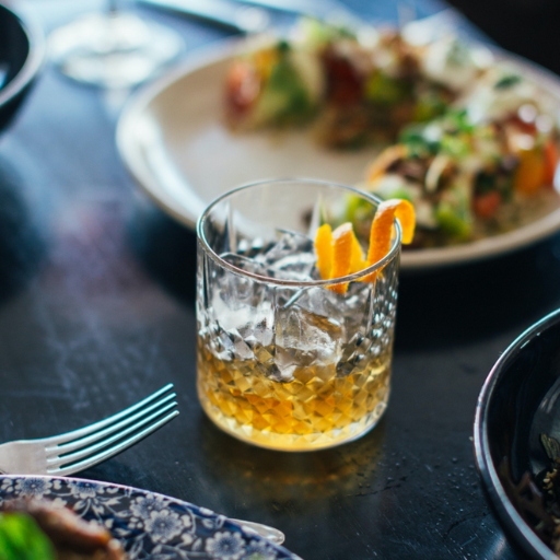 Glass filled with whisky with plates of food in the background 