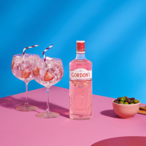Bottle of Gordon’s Premium Pink gin beside two G&T glasses against pink and blue background