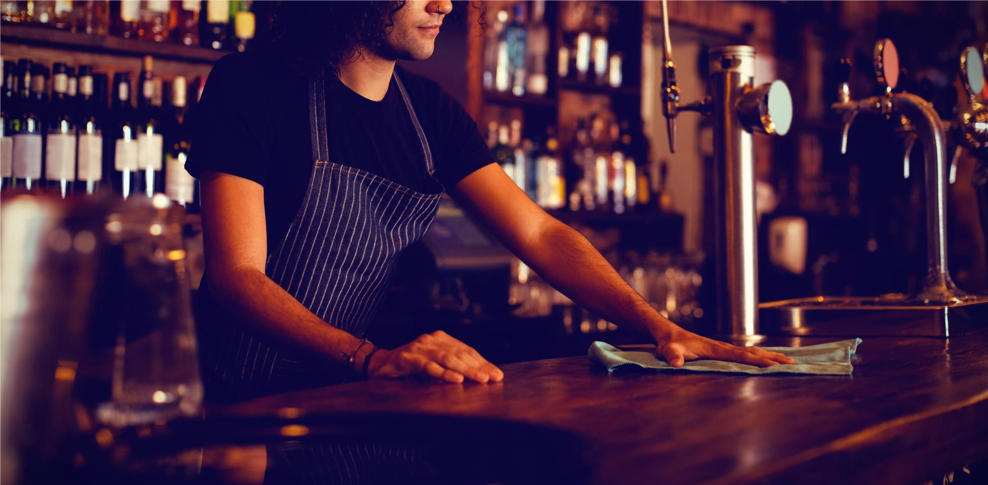 Personal del bar trabajando detrás de una barra ocupada con clientes sentados en la barra con comida y bebidas.