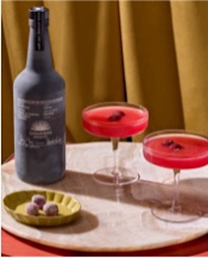 Zwei Gläser Mezcal neben einer dunklen Flasche und Stachelbeeren