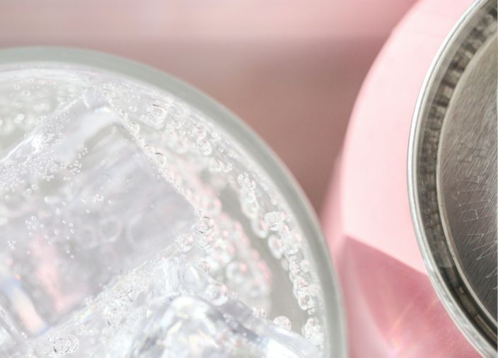 Copo com líquido gaseificado ao lado de uma lata sobre um fundo rosa 