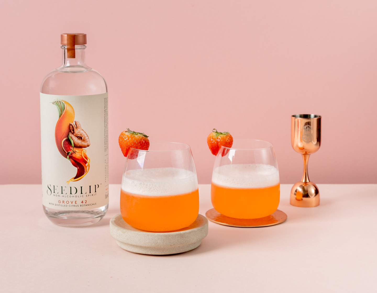 Seedlip Grove 42 com fundo rosa e dois coquetéis com guarnição de morango