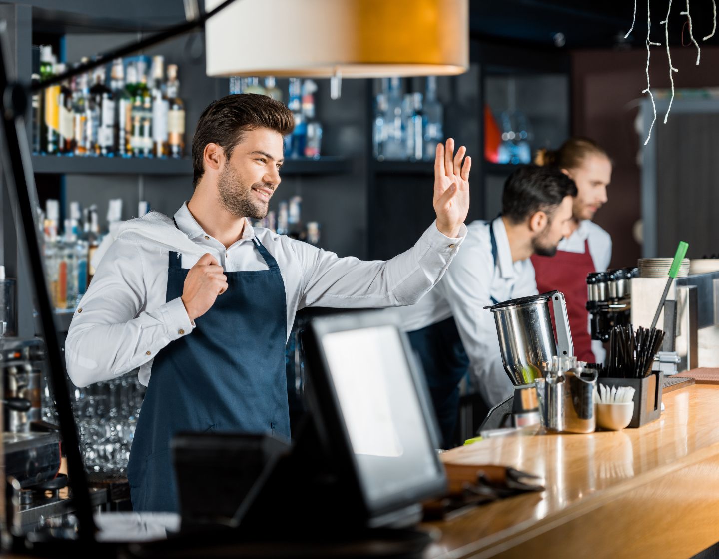 Bartender recebendo um convidado no bar com um sorriso e linguagem corporal positiva.