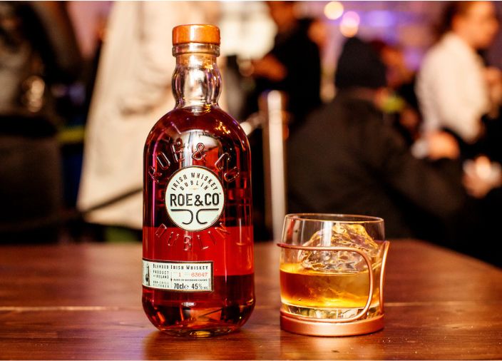 A bottle of Roe & Co with whiskey glass filled with whiskey serve and ice.