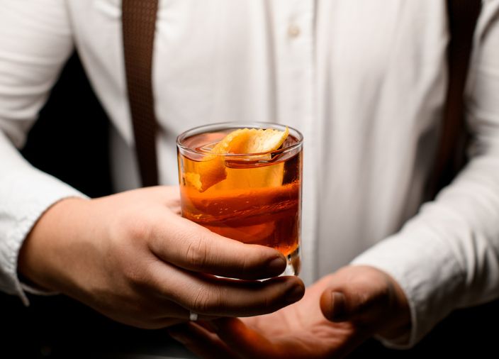 Bartender in white shirt holding a clear cocktial with orange garnish.