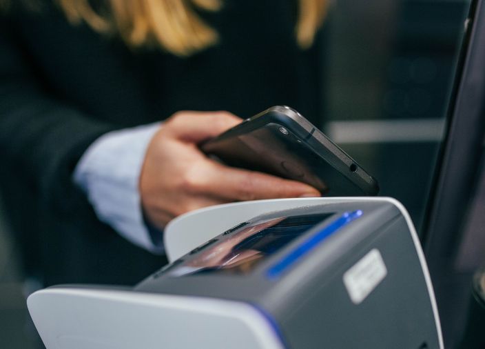 Una mujer toca para pagar con su teléfono en una terminal POS.