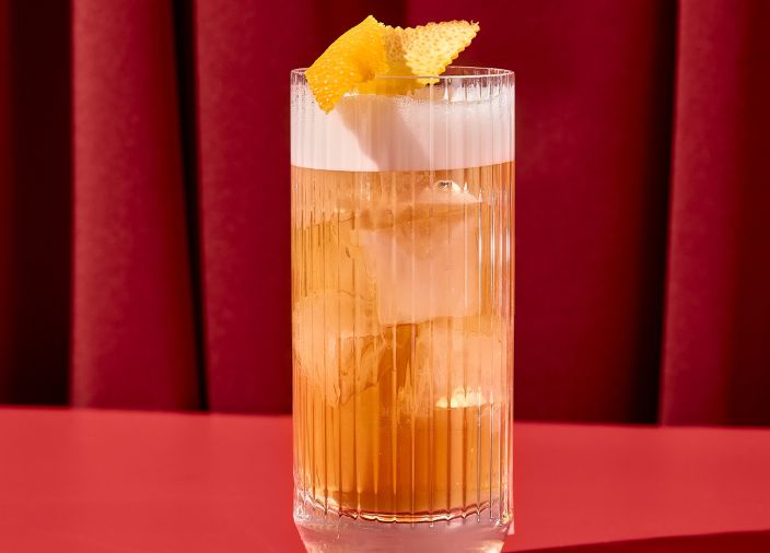 Orange whiskey cocktail in highball glass garnished with fruit.