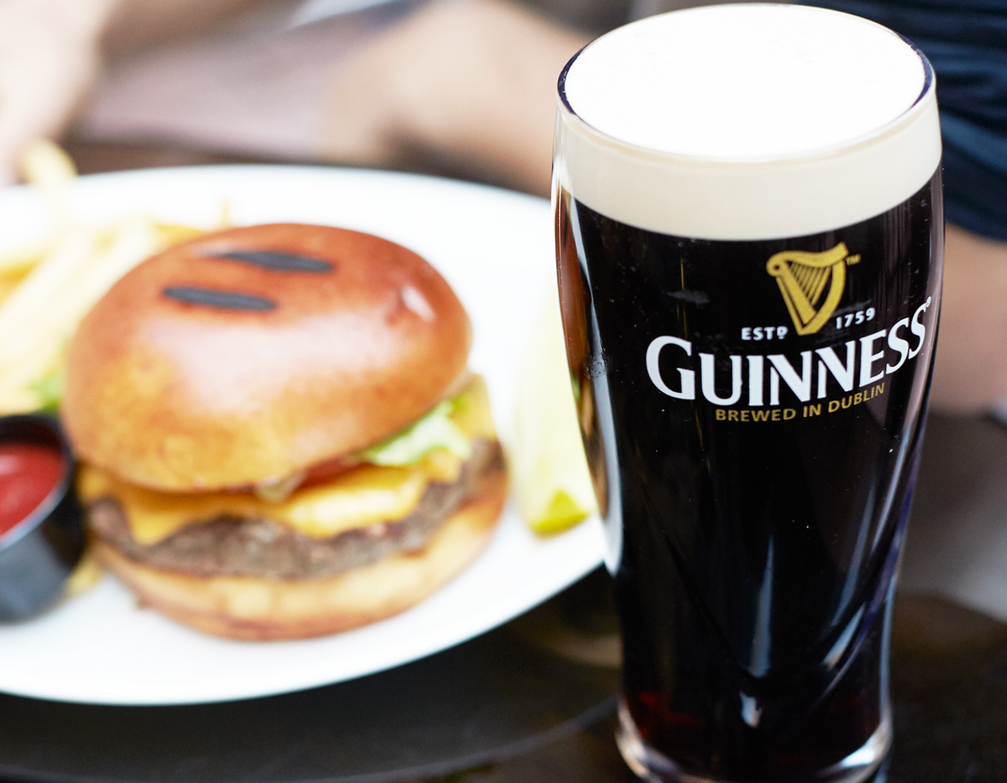 Pinta de Guinness en la mesa con hamburguesa y patatas fritas detrás