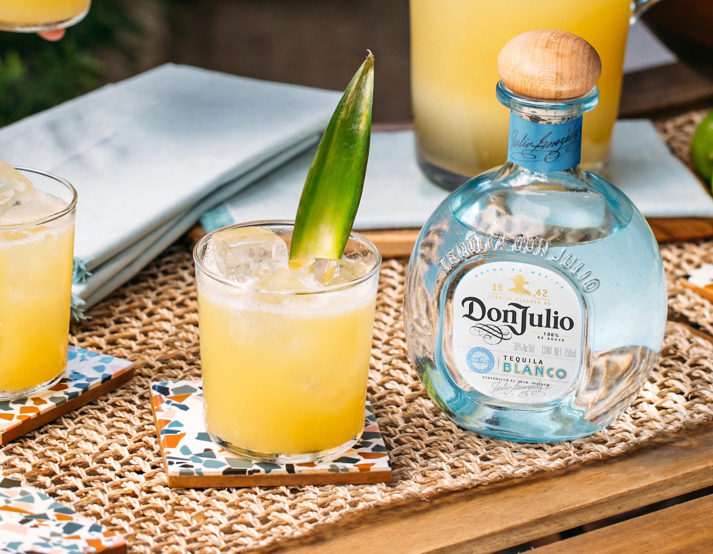 Botella de Don Julio Tequila Blanco junto a un cóctel aderezado con una hoja.