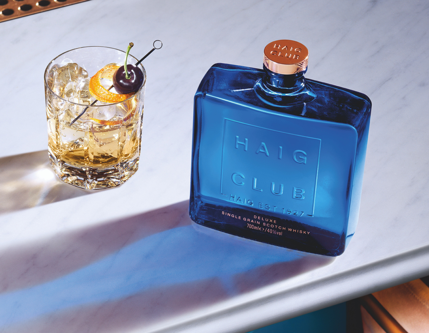 Botella de Haig Club Single Grain Scotch Whisky junto a un cóctel. 
