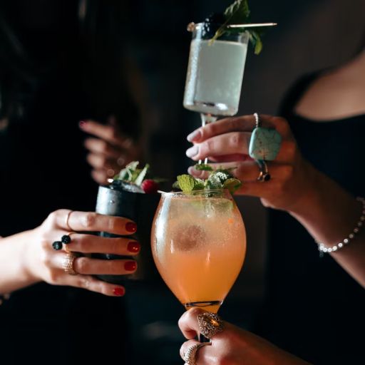 Una selección de diferentes cócteles a base de ginebra dispuestos juntos sobre una mesa blanca. Decorados con frutas y hielo, junto a una coctelera.