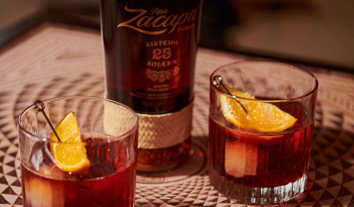Two drinks glasses garnished with lemon accompanied by a spirit bottle