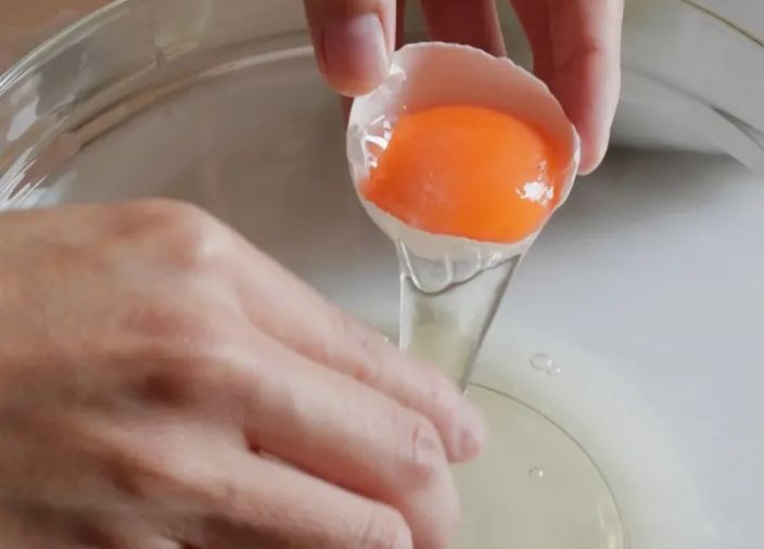 Person cracking egg into a bowl and separating egg whites