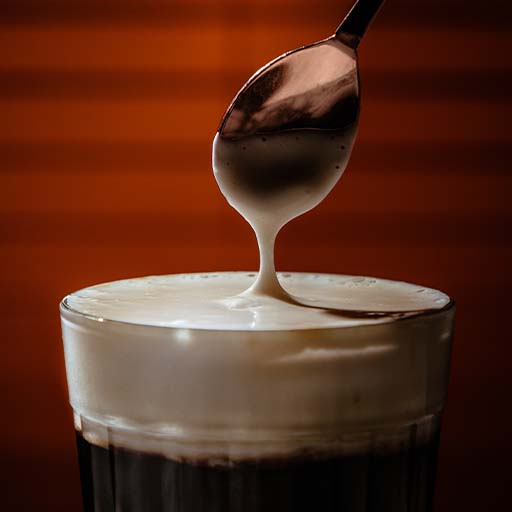 Un primer plano de una cuchara para revolver sobre la parte superior de una bebida con una capa gruesa de crema/espuma encima. 
