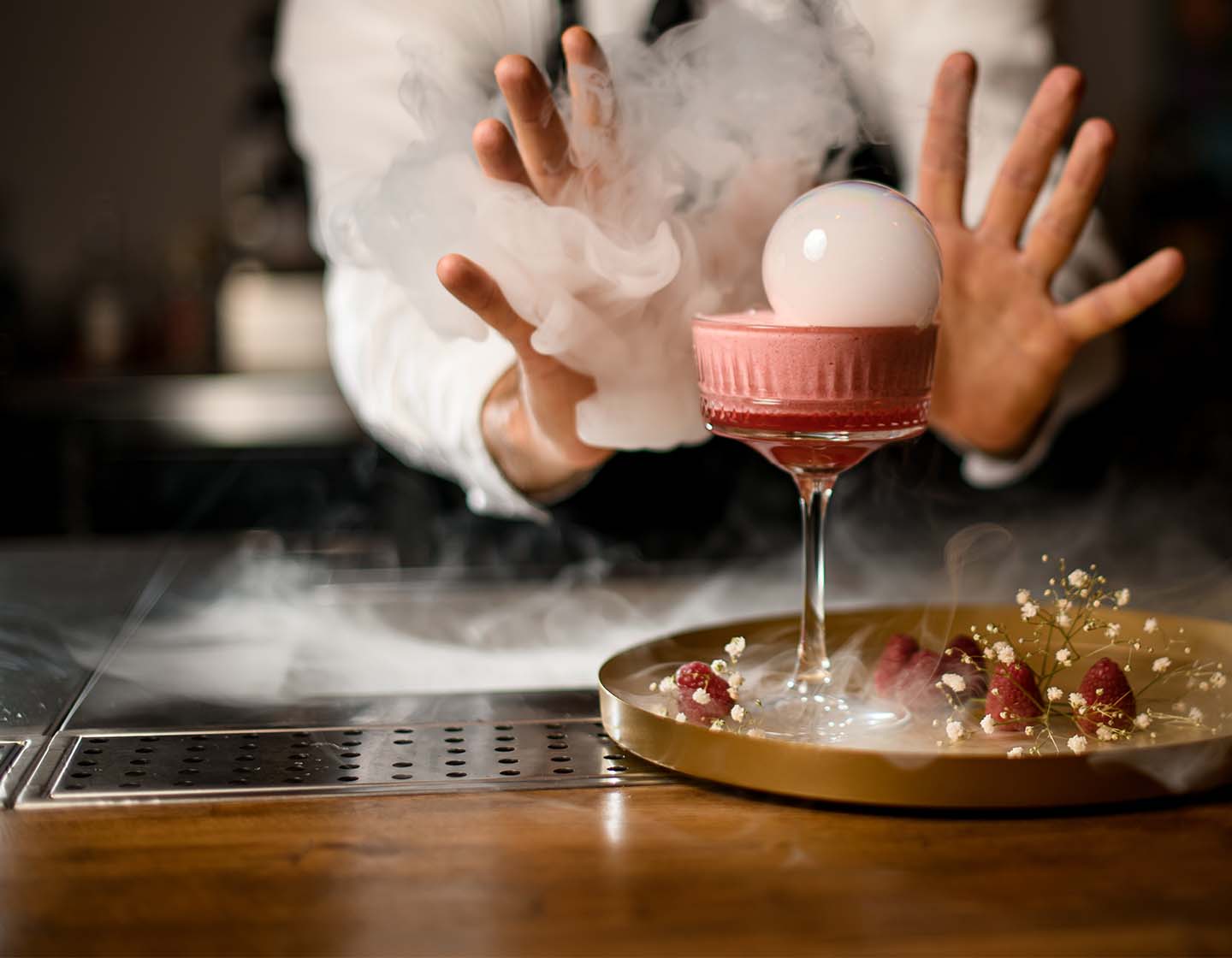Ein Barkeeper präsentiert einen Cocktail, der von Nebelschwaden umgeben ist.