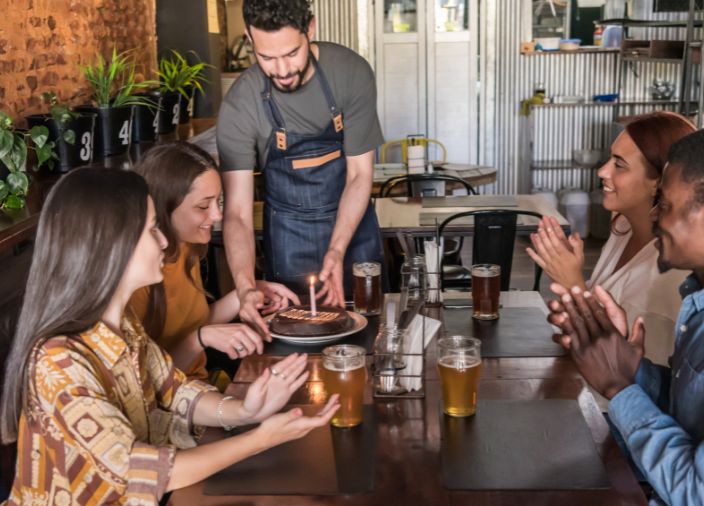 Um convidado sorrindo enquanto o bartender entrega uma pequena fatia de bolo com uma vela