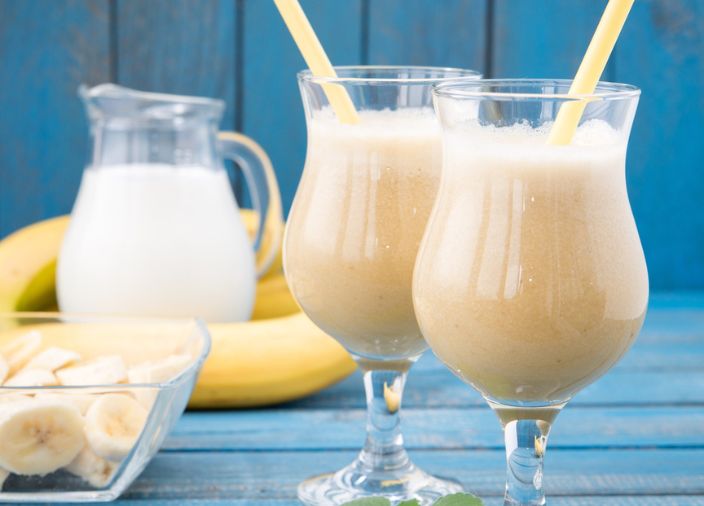 Dois copos de bebida de banana misturada acompanhados de bananas picadas