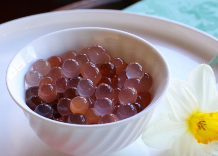Spheres in different shades of pink in a white bowl next to a dandelion.