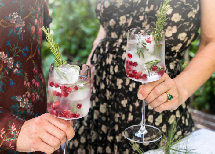  Two people holding cocktails with sprigs and cranberries