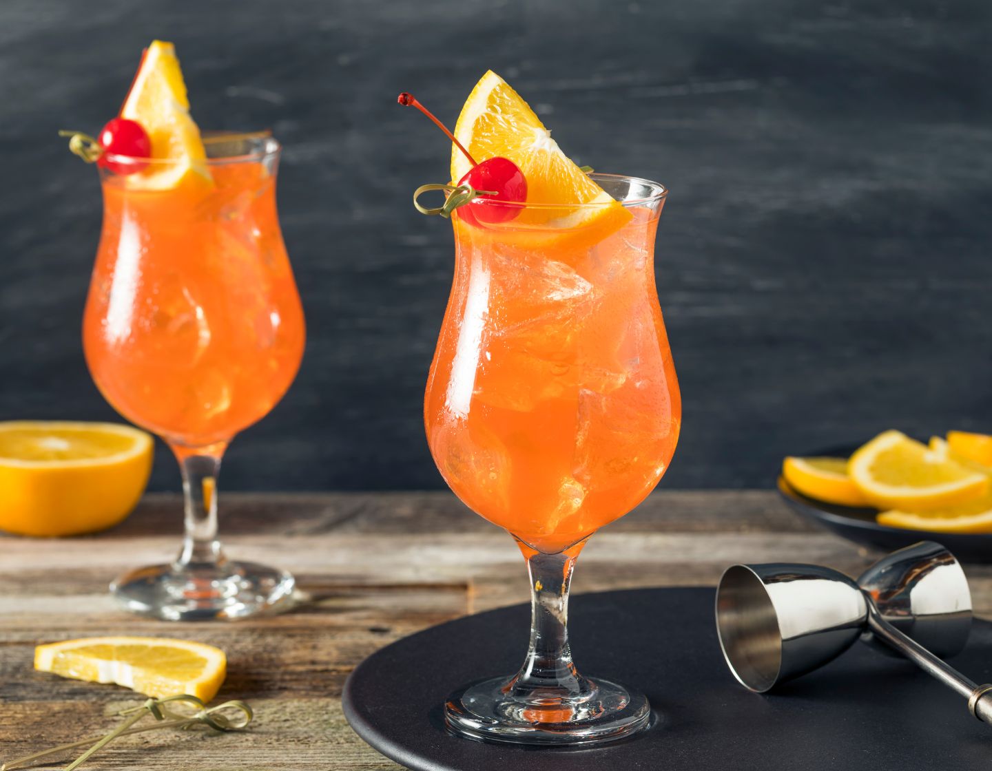 Dos Singapore Slings rodeados de rodajas de naranja y adornados con una cuña de naranja y una cereza.