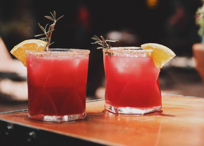 Zwei rote Drinks mit Garnierung stehen auf einem Holztisch