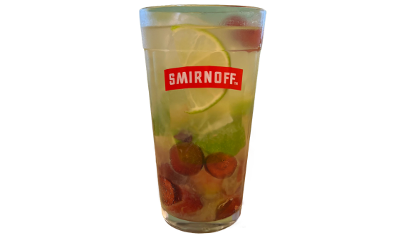 Copo alto com logo vermelho da Smirnoff contendo um coquetel claro e refrescante. A bebida é misturada com gelo, várias metades de uva rubi no fundo e decorada com uma rodela de limão verde no interior. Fundo branco isolado.