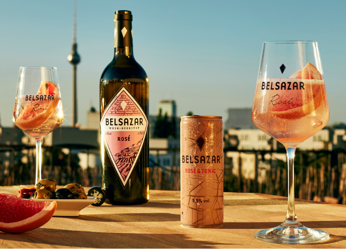 Botella de Belsazar rosé en una mesa al aire libre al atardecer junto a dos copas de vino llenas de bebidas rosadas