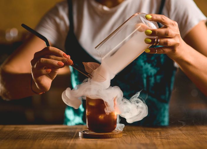Una copa de cóctel rodeada de humo, mientras el bartender arregla el garnish.