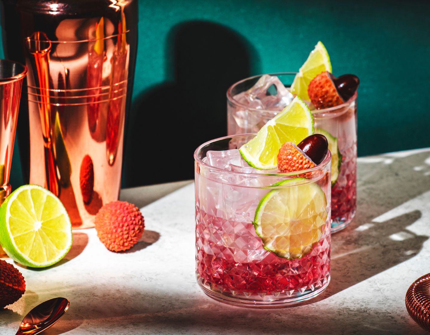 two tequila cocktails with lime garnish beside cocktail shaker
