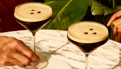 2 espresso martinis on a tsble with hands reaching