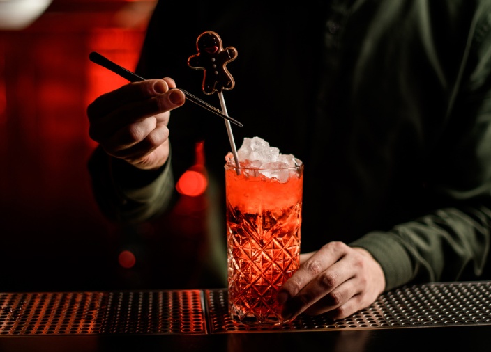 A bartender adding a gingerbread man garnish to a red cocktail with ice.