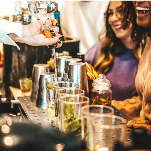 Bartender pouring cocktails infront of customers at a bar.