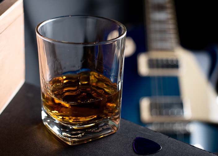 Um copo de whiskey com um violão embaçado ao fundo