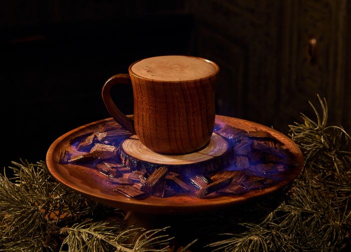 A hot chocolate cocktail in a wooden mug and a rustic wooden plate.