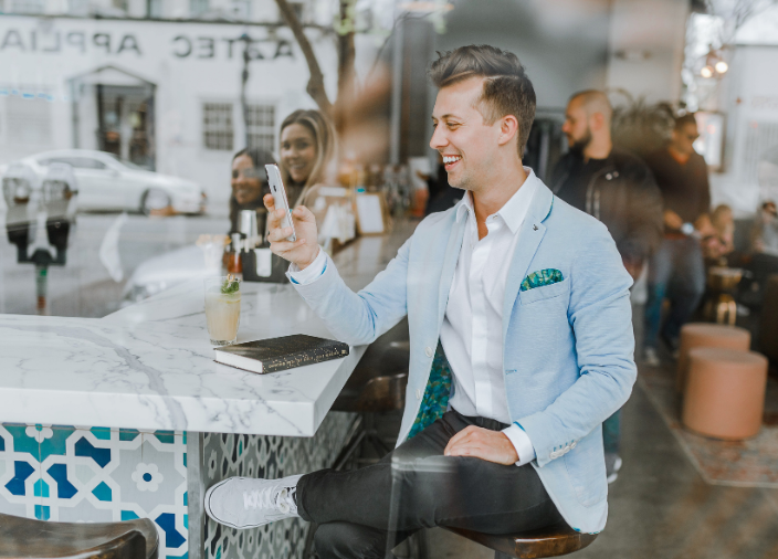 Un hombre en un bar con un libro y un cóctel sosteniendo un teléfono