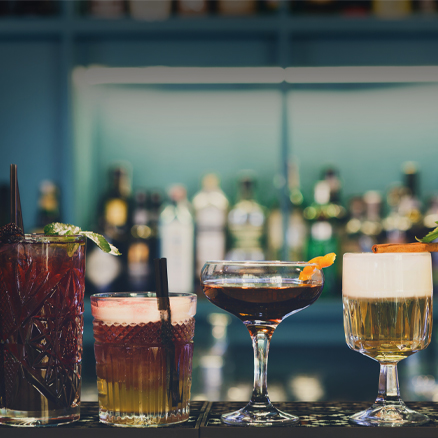 Four different garnished cocktails lined along a bar.