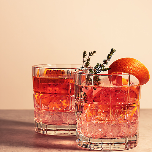 Carbonated cocktail of red colour with orange garnish 