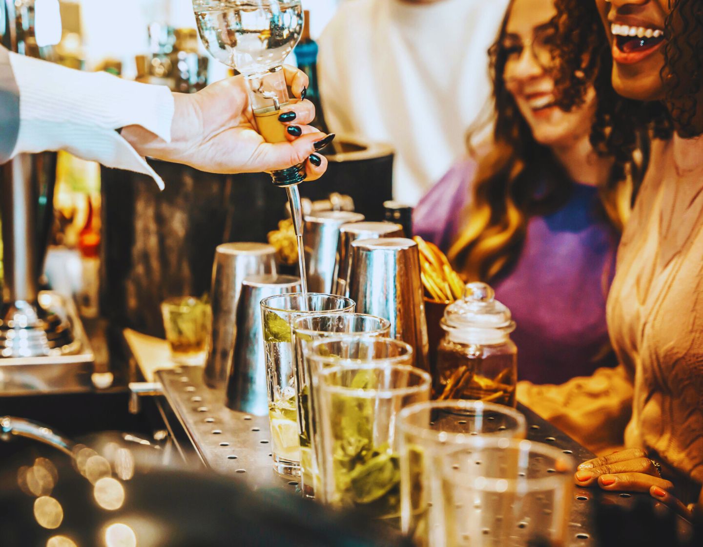Barkeeper mixt Drinks, Gäste lachen