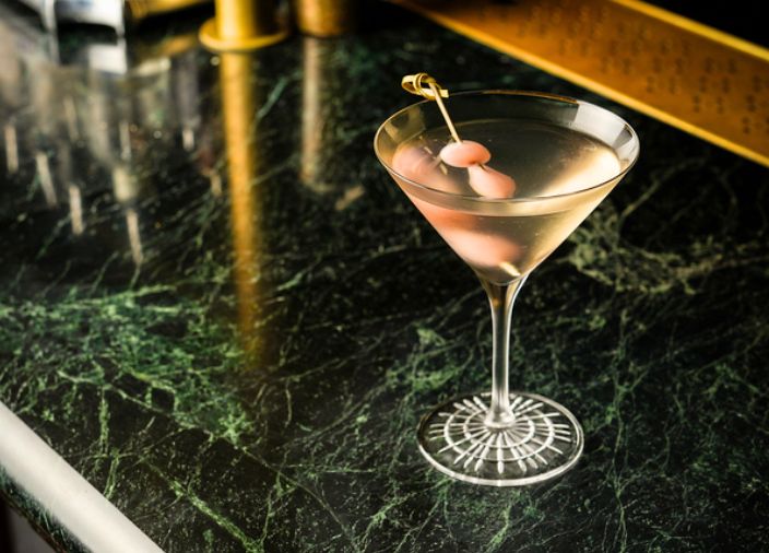 A martini drink with a pink pickle garnish.