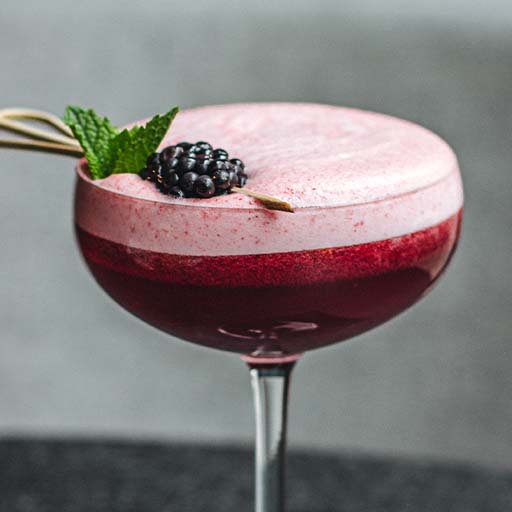 A cocktail with foam on top, garnished with a blackberry
