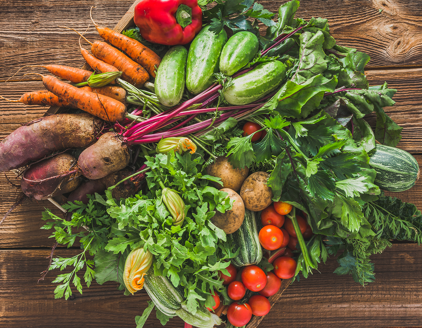 Una colección de verduras, zanahorias, remolachas, pepinos, tomates, calabazas y más, reunidas en círculo encima de una mesa de madera.