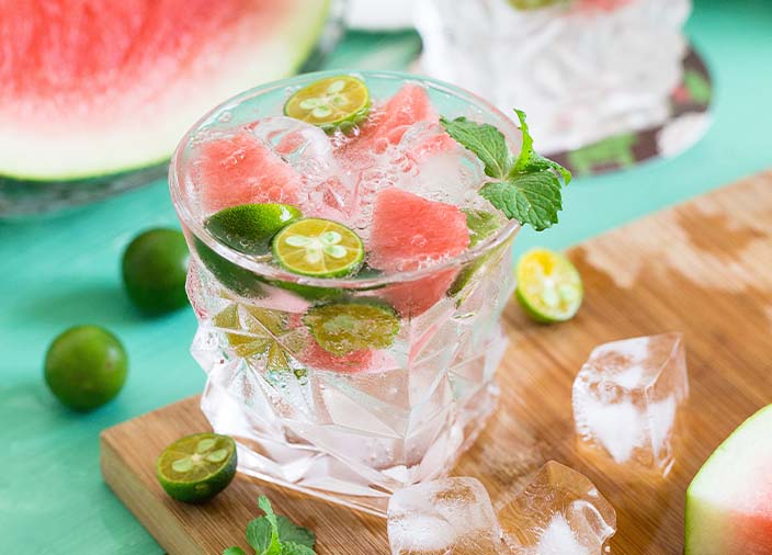 A clear glass filled with liquid garnished with green chillies and watermelon 
