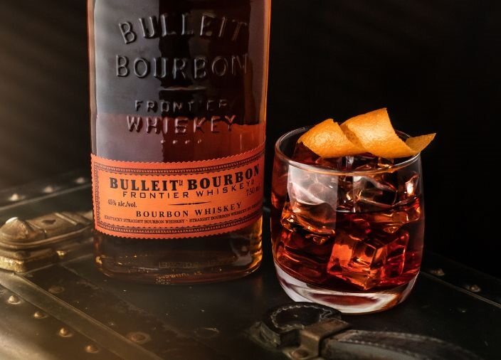 Eine Flasche Bulleit Bourbon mit einem garnierten Glas auf einer Holzfläche