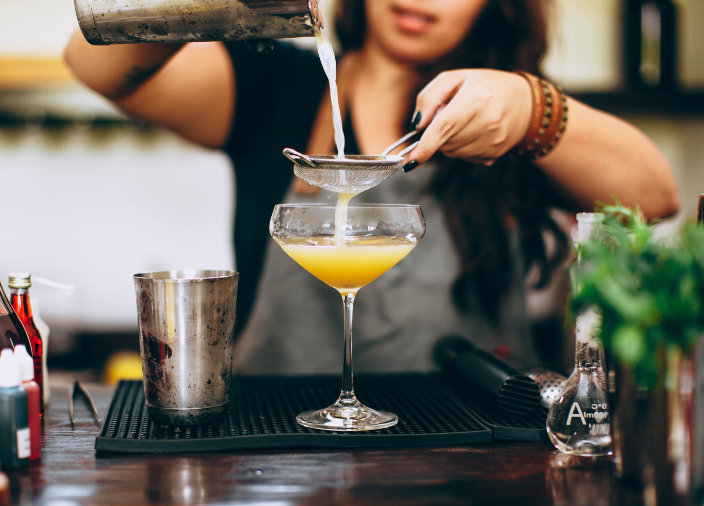 Eine Barkeeperin gießt einen Cocktail durch ein Sieb.