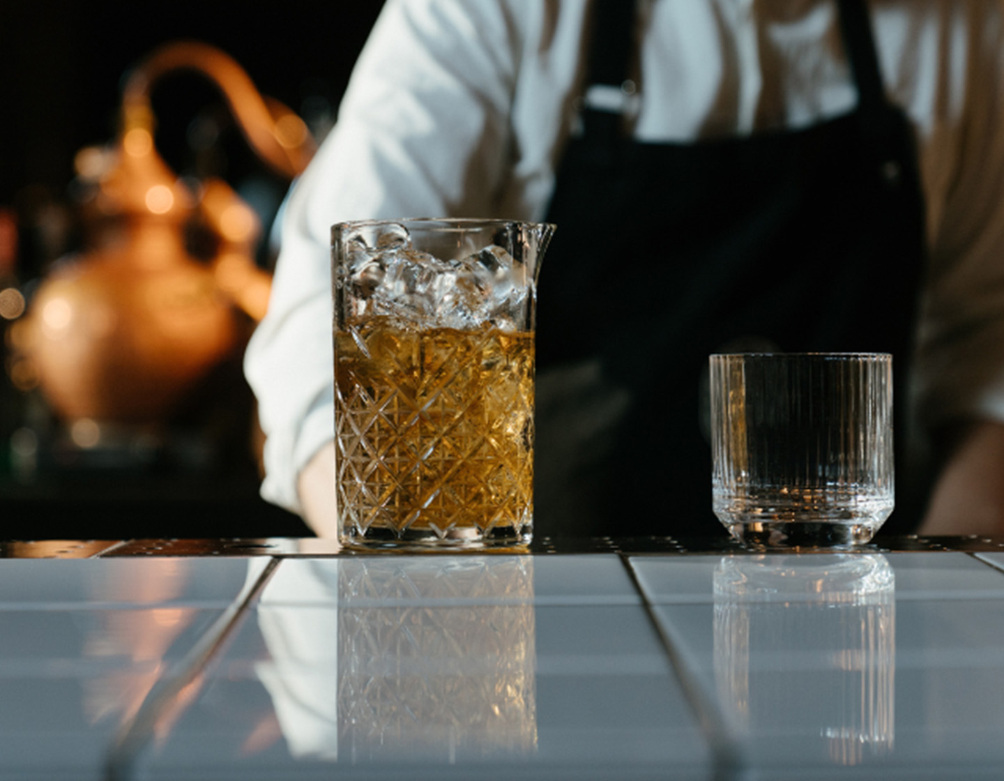 Bartender de pie detrás de un vaso mezclador lleno de líquido y un vaso vacío