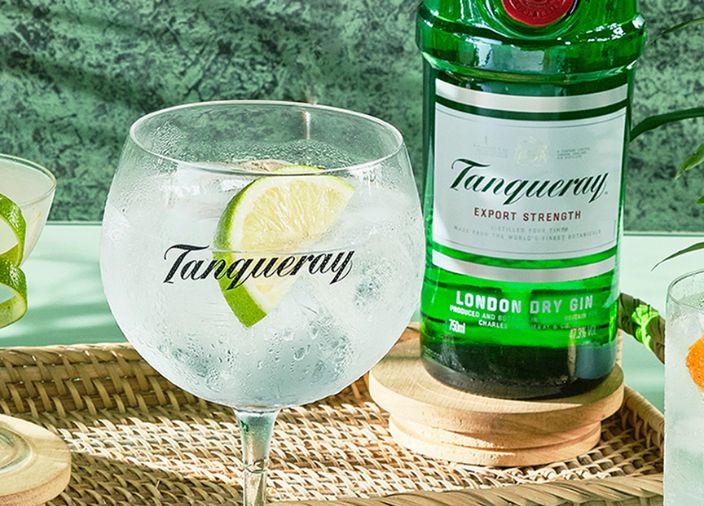 Uma taça de gim recheada com guarnição de limão ao lado de uma garrafa de Tanqueray.